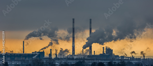 A panorama of a steel plant against the background of the orange sky. Smoking chimneys  environmental poisoning. Picture taken on a cloudy day  dramatic light.