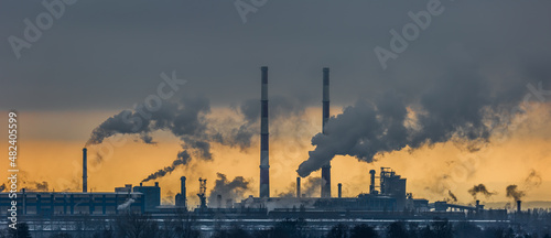 Obraz na płótnie A panorama of a steel plant against the background of the orange sky. Smoking chimneys, environmental poisoning. Picture taken on a cloudy day, dramatic light. w salonie