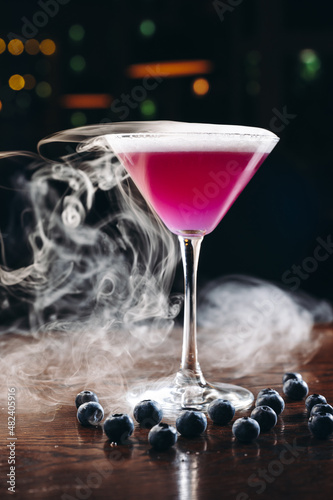 Smoking martini glass with purple drink. Cocktail with blueberries 