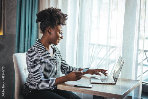 Young woman holding credit card and using laptop computer. Businesswoman working at home. Online shopping, e-commerce, internet banking, spending money, working from home concept