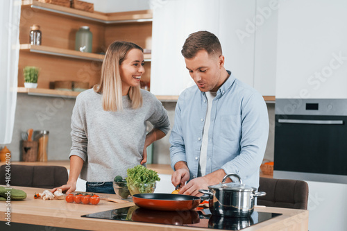 Talking with each other. Couple preparing food at home on the modern kitchen