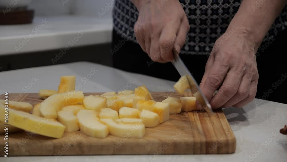 Slicing zucchini on a wooden board on a white table with a large chef's knife. A woman is dicing vegetables in close-up. Slicing zucchini on a wooden board on a white table with a large chef's knife. A woman is dicing vegetables in close-up.