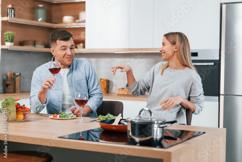 With glasses of wine. Couple preparing food at home on the modern kitchen
