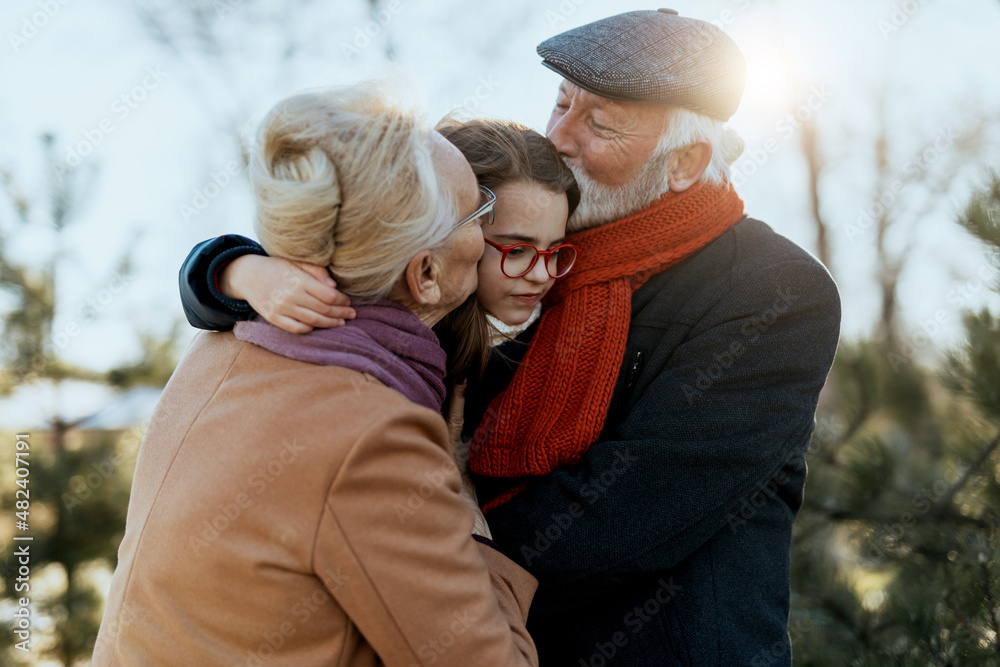 Fototapeta premium Grandma and grandpa enjoy with their sweet granddaughter on a sunny winter day.