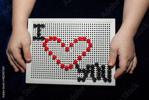 hands of a little girl holding puzzles with the inscription I love you. Red heart lined with mazaika on February 14 Valentine's Day photo