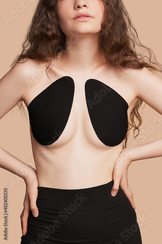 Cropped shot of slim brown-haired lady in black skirt and black adhesive bra for breast lift. Thin cotton bra is invisible under backless or strapless dresses. photo