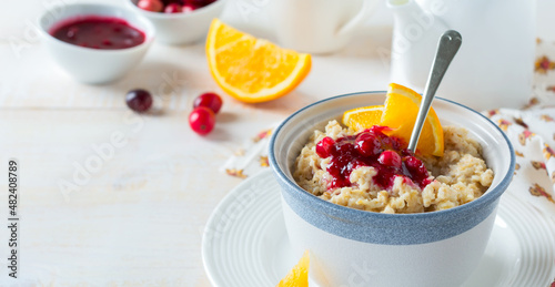 Oat porridge with cranberry sauce and orange in a ceramic bowl for healthy breakfast on a light background. Selective focus.