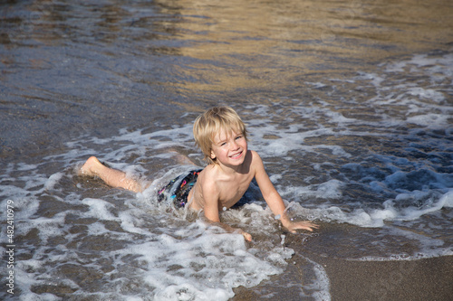 happy cheerful child, boy 4-5 years old, lying on the seashore. The kid has fun on coast during the summer holidays. the concept of a healthy lifestyle and recreation. Happy childhood, hello summer