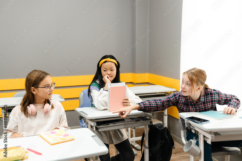 Fototapeta premium Multiracial girls talking and sitting at desks during class