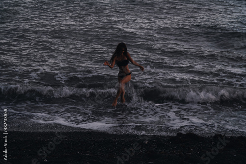 Fototapeta Naklejka Na Ścianę i Meble -  happy girl in a swimsuit happily runs along the sea waves on beach on summer evening. Photo with a blur from a long exposure to give an authentic atmosphere
