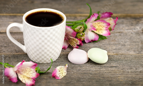 Cup of coffee, flowers and meringue on a wooden textured table. Sweet breakfast