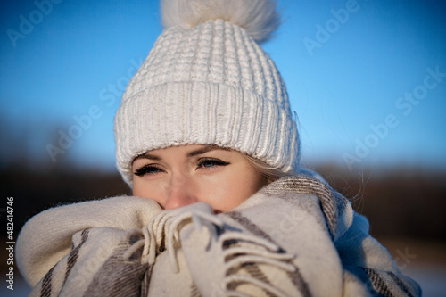 portrait of a young woman in the forest on a sunny winter day, a woman in a knitted hat and a warm plaid