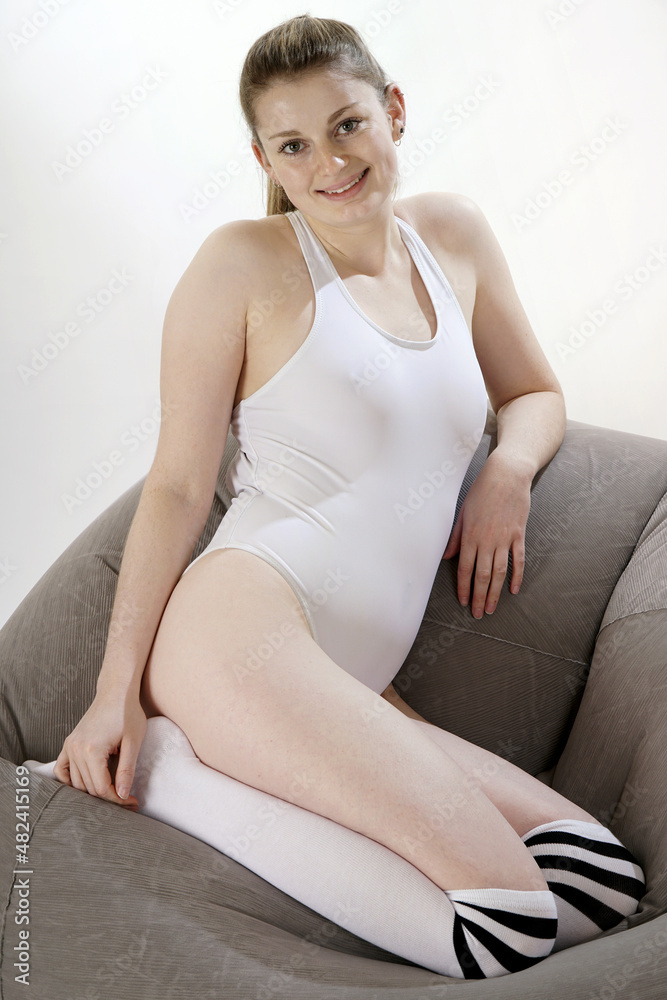 Obraz premium Beautiful young woman in white one piece swimsuit posing on a sofa in studio