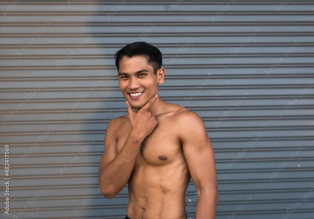 Fototapeta premium Young man with fit and firm muscle,raise finger touch chin,happy feeling,