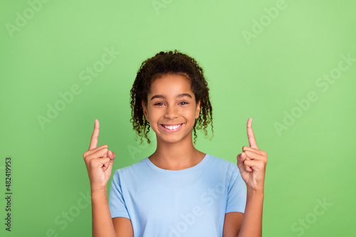 Portrait of attractive cheerful girl demonstrating up copy space place ad advert isolated over green pastel color background