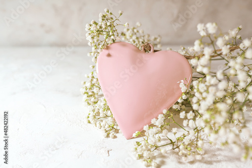 Rose colored heart shape and white gypsophila flowers on a light rustic background, love concept for valentines od mothers day, copy space, selected focus