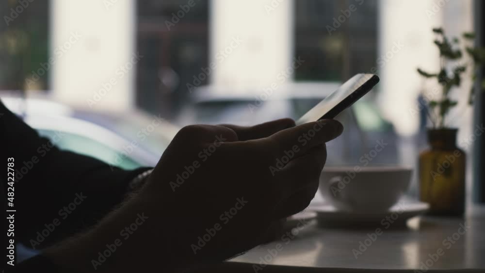 Close up side view millennial man holding cellphone, swiping photos in  dating app. Young man ordering food taxi in mobile application, web surfing typing message in social networks
