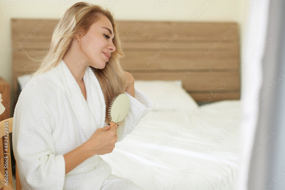 Positive young woman brushing hair in the morning after waking up Positive young woman brushing hair in the morning after waking up