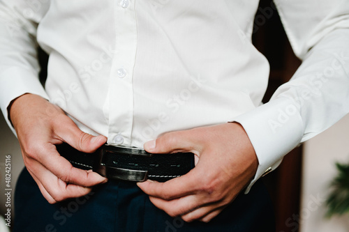 A man in pants and shirt buttoned a black leather trouser belt. Groom Dress up a belt with buckle. Businessman wear leather stylish belt. New classic belt.