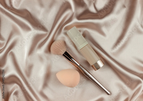 Face Foundation and brush,on a beige silk pastel background,make up,flat layot