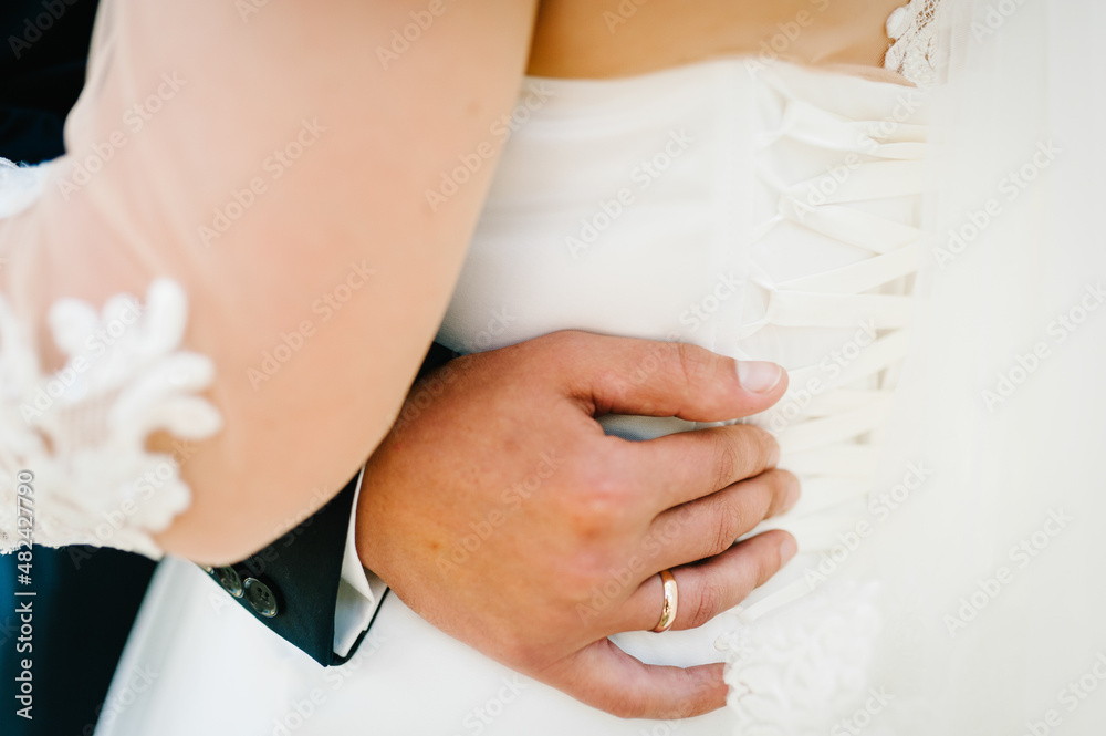 The groom embraces the bride with his hands behind the waist and standing on wedding ceremony of the outdoor in the nature backyard. The groom embraces the bride with his hands behind the waist and standing on wedding ceremony of the outdoor in the nature backyard.