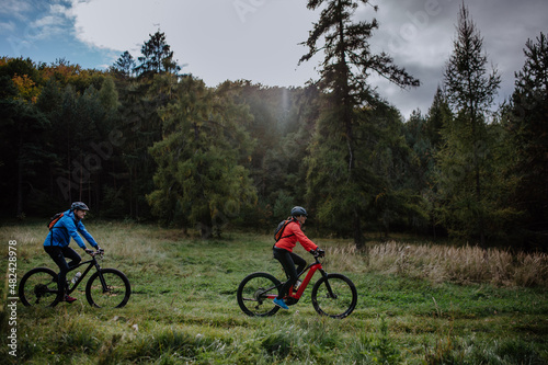 Side view of active senior couple riding bikes outdoors in forest in autumn day.