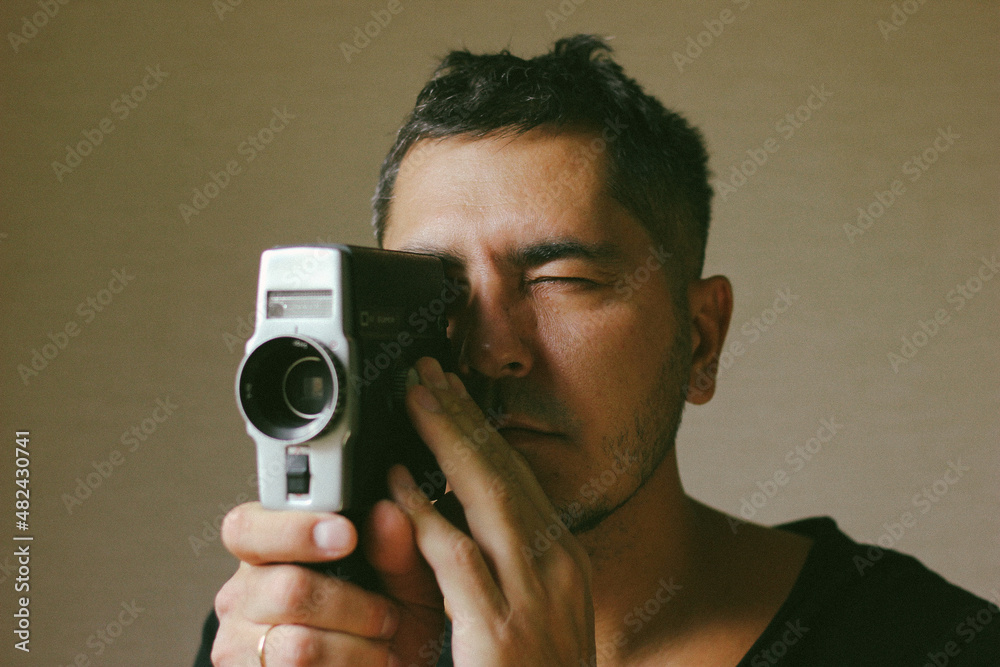 Young rapper man excited and entertained, looking through a film camera, recording a movie Young rapper man excited and entertained, looking through a film camera, recording a movie