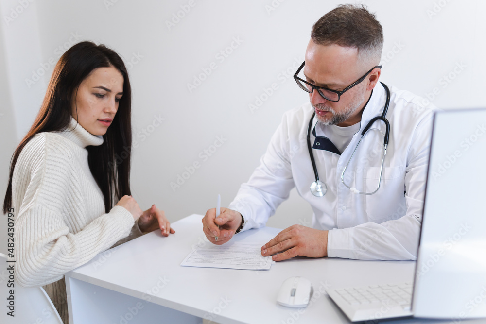 Doctor writes a prescription for medicines to his patient. Woman at the medical appointment Doctor writes a prescription for medicines to his patient. Woman at the medical appointment