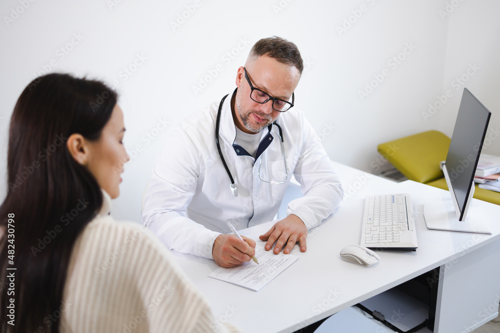 Doctor writing on a prescription note in medical office. Woman at the doctor's appointment Doctor writing on a prescription note in medical office. Woman at the doctor's appointment