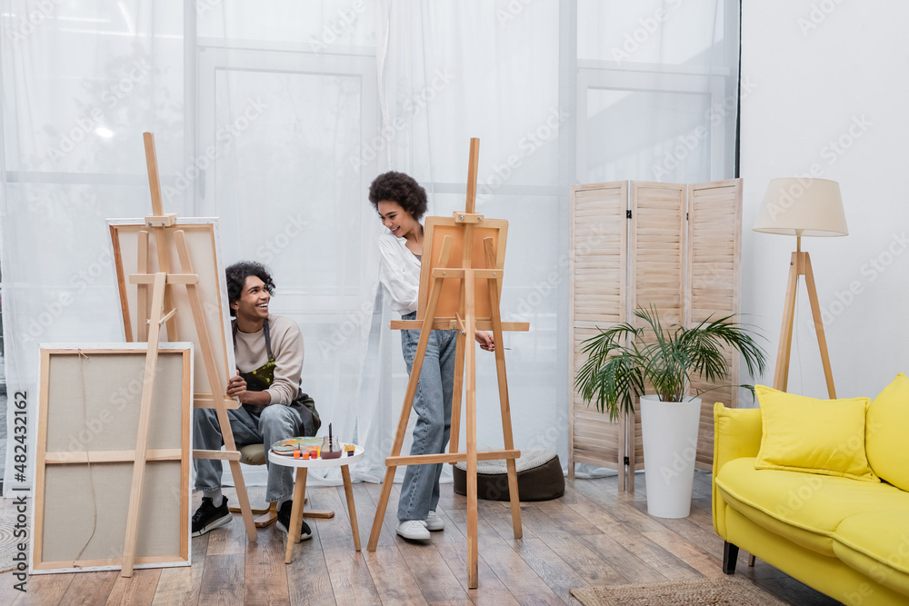 Positive african american couple looking at each other while painting on canvases at home. Positive african american couple looking at each other while painting on canvases at home.