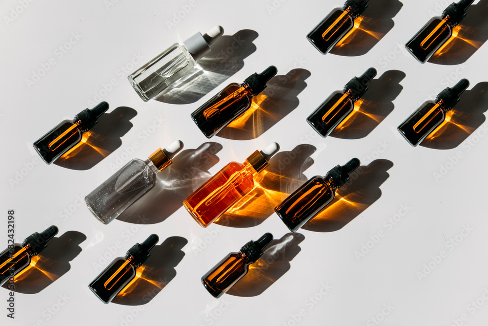 A set of many different glass bottles with cosmetic liquids arranged in a row. The play of light creates abstract patterns of shadows. A set of many different glass bottles with cosmetic liquids arranged in a row. The play of light creates abstract patterns of shadows.