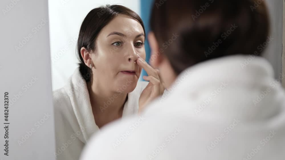 A woman looking at herself in the mirror corrects her makeup, looking for wrinkles. The girl admires herself and is concerned about her appearance. A woman looking at herself in the mirror corrects her makeup, looking for wrinkles. The girl admires herself and is concerned about her appearance.