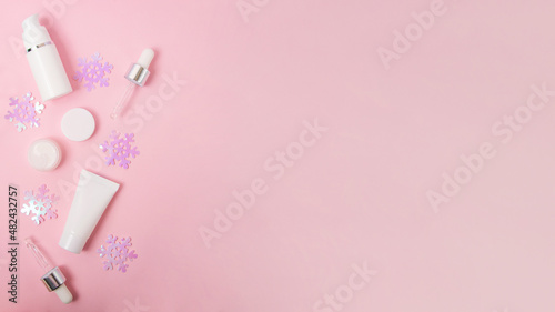 Composition from blank cosmetics containers and glittering snowflakes on the pink background with snow.Large banner with copy space. © Bidzilya