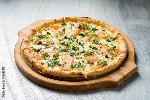 Pizza with salmon, cheese and green onion on the board on grey table