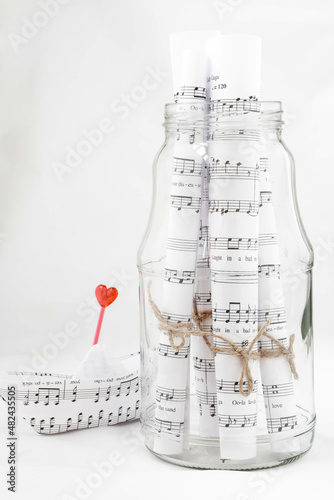 Moscow, Russia, January 2022, sheet music tied with twine in a glass jar on a white background, next to a paper boat folded from notes