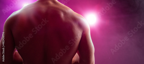 Hombre musculoso de espalda a la cámara Espalda musculosa desnuda a contraluz. Iluminación colorida. Concepto evento deportivo, fitness, físico culturismo, Boxeo. Espacio para texto.  photo