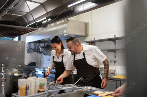 Happy chef and cook working on their dishes indoors in restaurant kitchen. photo