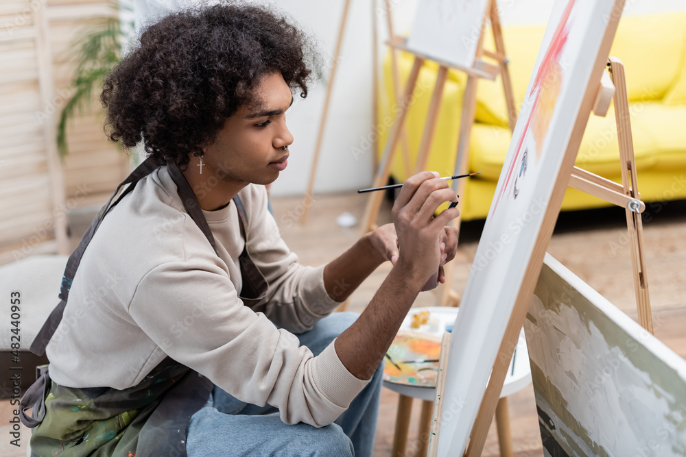 Young african american man painting on canvas at home.