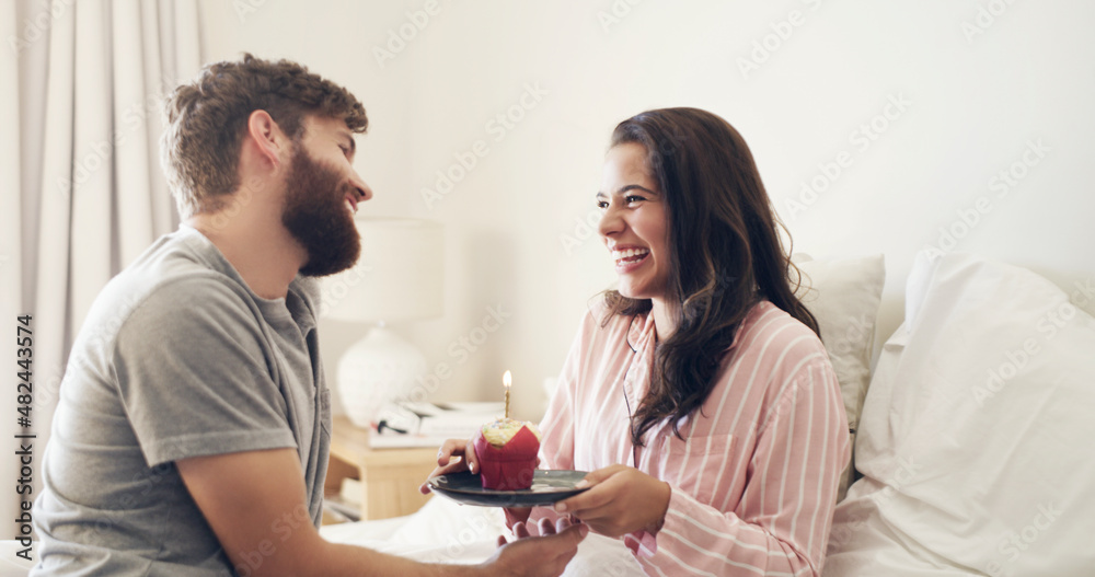 happy birthday to my beautiful wife. Shot of a young man surprising his wife with a cupcake in bed at home. happy birthday to my beautiful wife. Shot of a young man surprising his wife with a cupcake in bed at home.