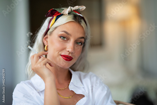 Portrait of a fashionable young woman wearing hair scarf and white shirt while smoking cigarette