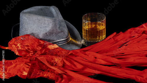 Foto Red babydoll in veil, gray man's hat and glass of whiskey, on a black background