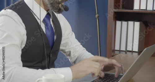 Bearded hipster businessman wearing eyeglasses and headset using devices at the office. People, modern technology, and rest concept.
