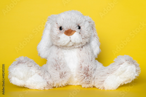 Stuffed soft toy bunny on yellow background. Easter concept. Beautiful white toy bunny sitting on colored background.