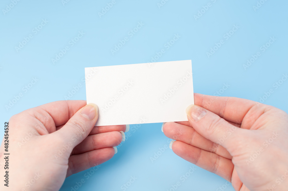 Female hands with a blank card isolated on blue background. Hands with empty white card. Mock up Female hands with a blank card isolated on blue background. Hands with empty white card. Mock up