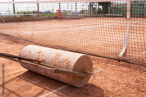 Heavy roll levels out clay tennis court on sunny day outdoors. Sport tournament maintenance concept