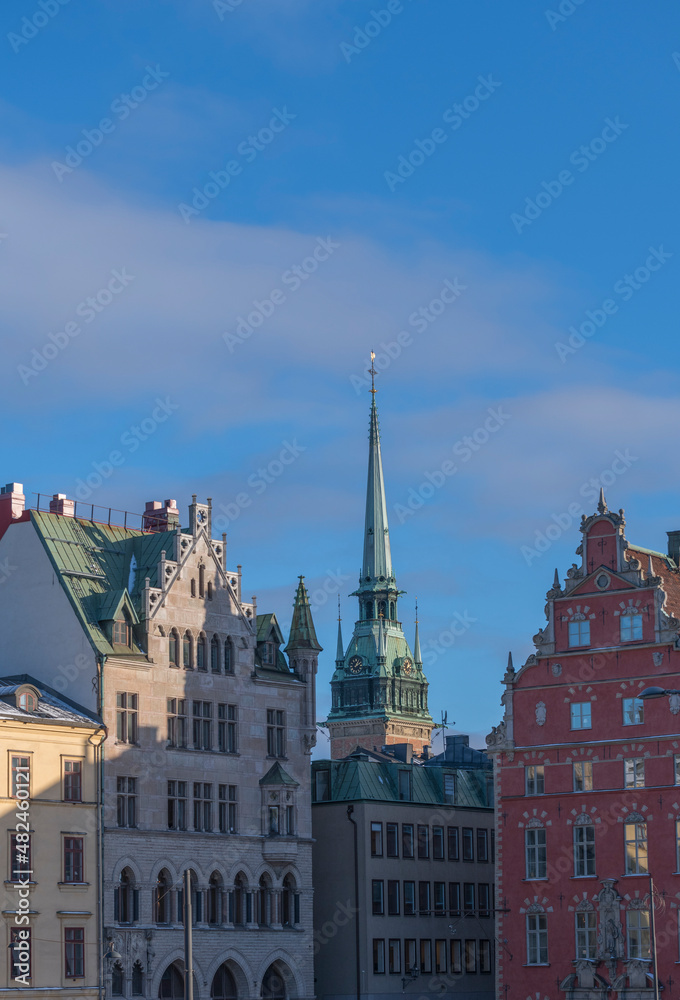 Obraz premium The tower of the German church Tyska Kyrkan between old 1700s building in the old town Gamla Stan a sunny winter day in Stockholm