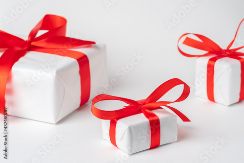 three gift packages with red ribbons, one in the foreground, two in a blur in the background