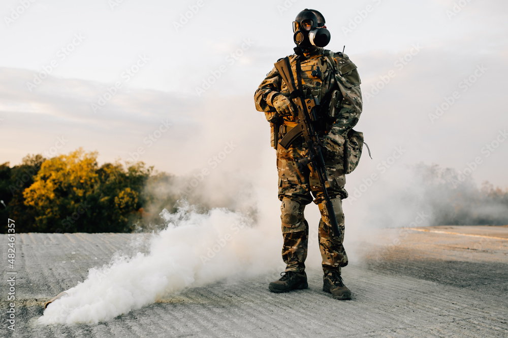 Soldier man standing on concrete in a gas mask next to a detonated smoke grenade on the street Soldier man standing on concrete in a gas mask next to a detonated smoke grenade on the street