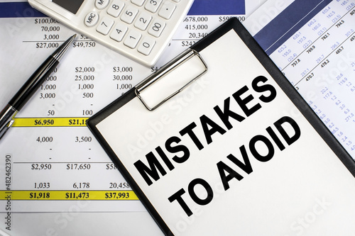 On the financial document near the white calculator lies a stationery tablet on which the inscription mistakes which should be avoided