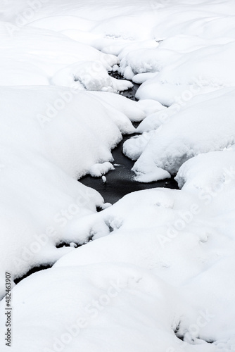 A frozen stream among the white snow. Snowy river. A washout on a snow-covered pond.
